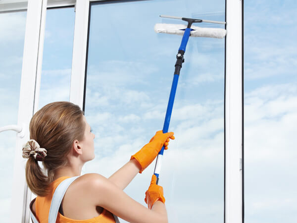 A lady using an extended pole and squeegee to clean a window